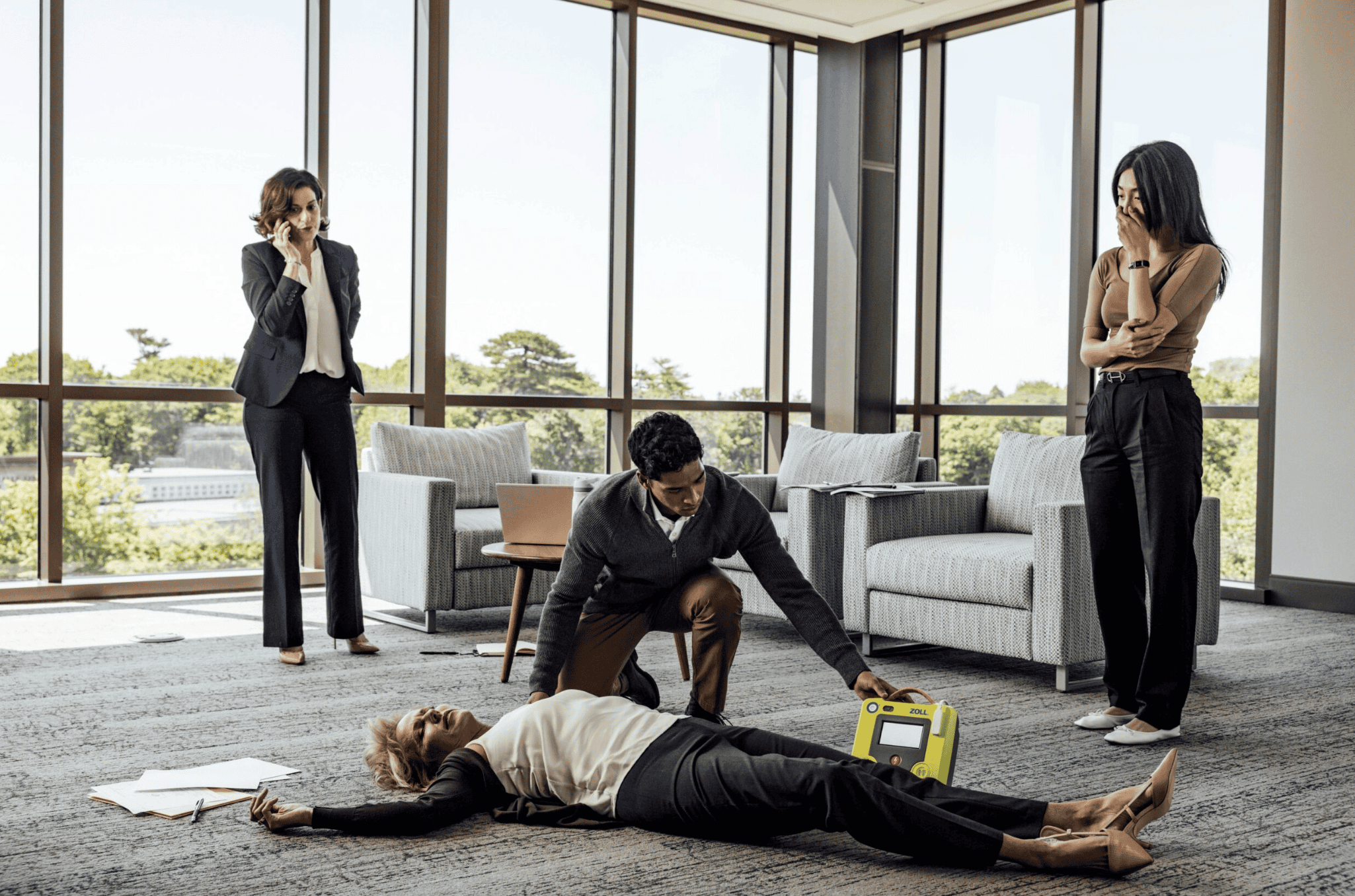 Une personne aide une femme allong&eacute;e au sol avec un d&eacute;fibrillateur.